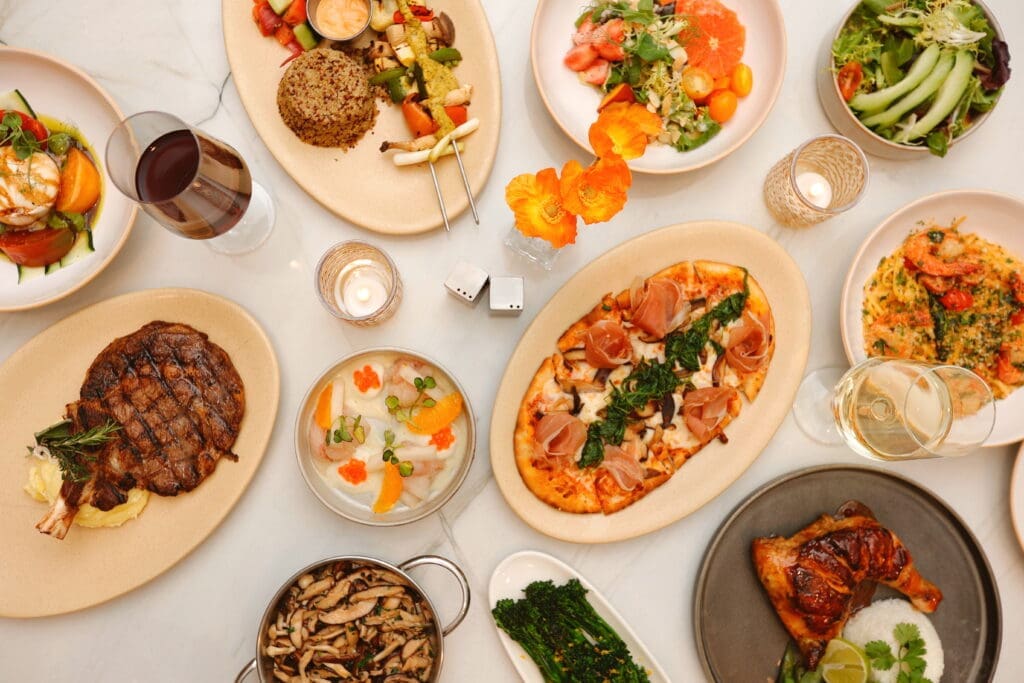Assorted dinner dishes at Poppy’s including steak, pizza, seafood, pasta and salads arranged on a marble table.