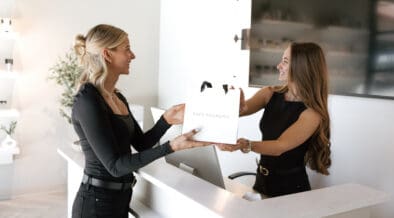 Minimal white reception desk at FACE FOUNDRIÉ Gilbert in SanTan Village featuring modern pendant lighting, a facial treatment menu board and clean contemporary design.