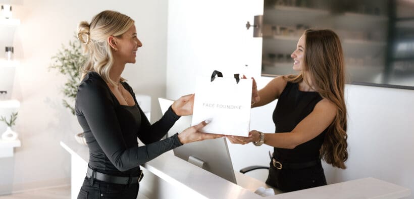 Minimal white reception desk at FACE FOUNDRIÉ Gilbert in SanTan Village featuring modern pendant lighting, a facial treatment menu board and clean contemporary design.