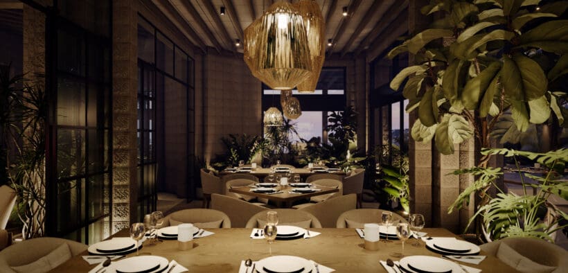 Interior dining room at Flying V Restaurant featuring wood tables set with white plates and wine glasses, woven statement chandeliers, stone walls and abundant indoor greenery under soft evening lighting.