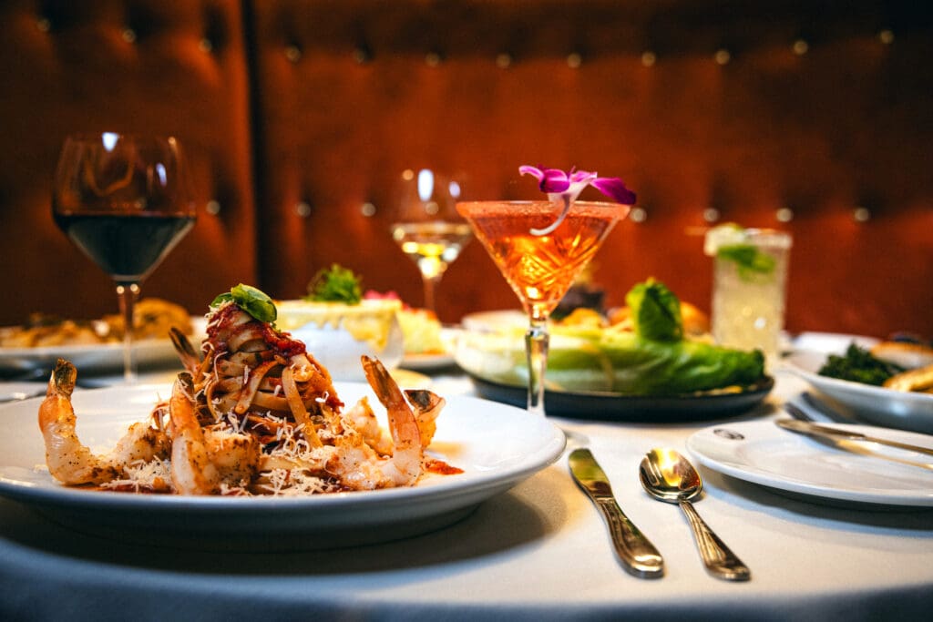 A romantic Valentine’s Day table set with plated seafood and steak dishes, wine glasses and cocktails inside Gregory’s Mesquite Grill at Eureka Casino Resort.