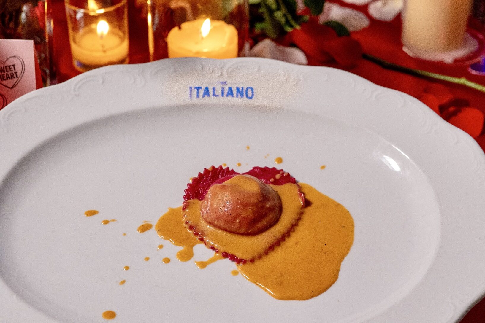 Red ravioli plated with creamy sauce at The Italiano in Scottsdale, Arizona, set against a candlelit Valentine’s Day table with roses and glowing votives.