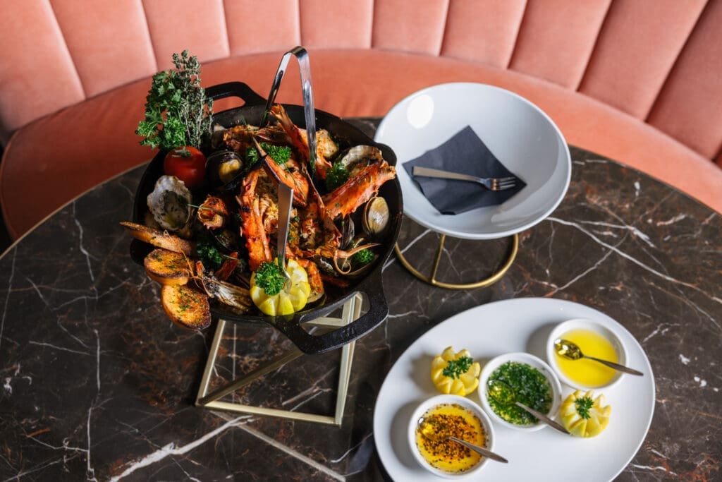 Josper roasted shellfish platter with king crab legs, lobster, prawns, clams and oysters served on a marble table with sauces and lemon.