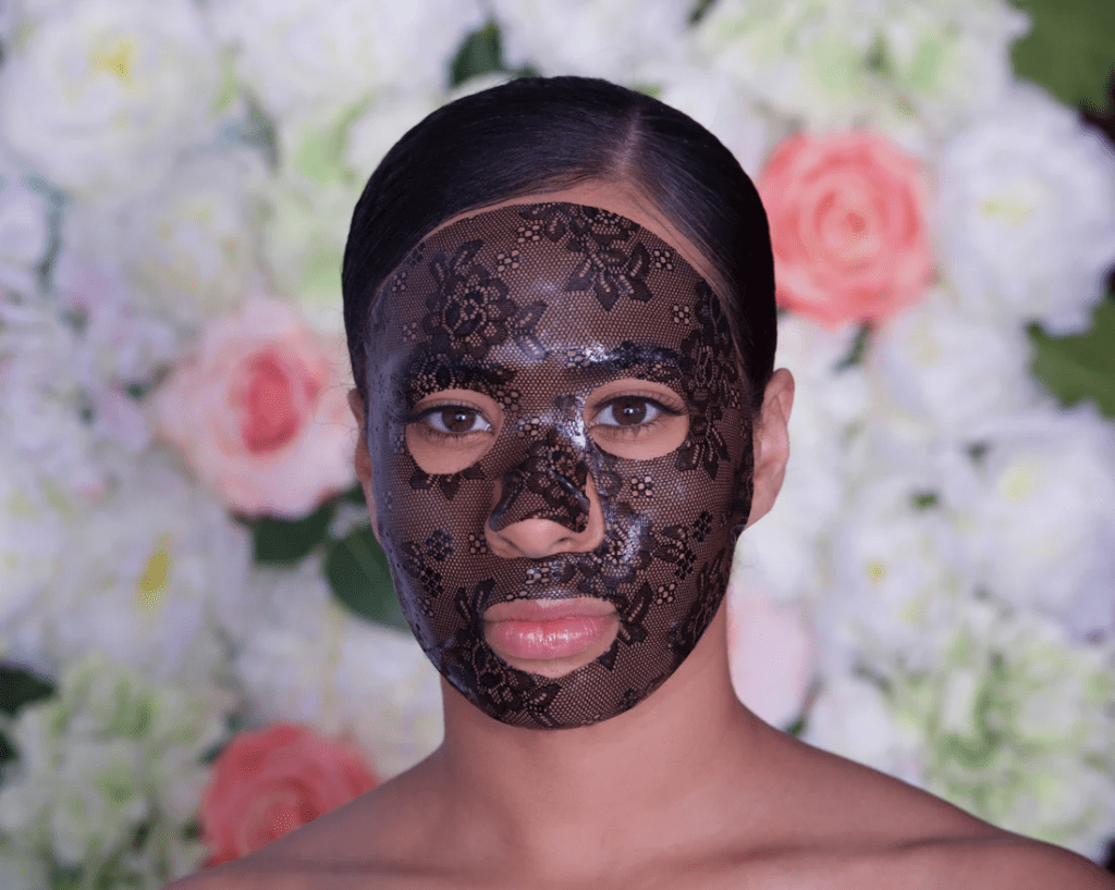 Model wearing the Lacial Masque hydrating sheet mask by Eve Milan NY, styled against a soft floral backdrop.