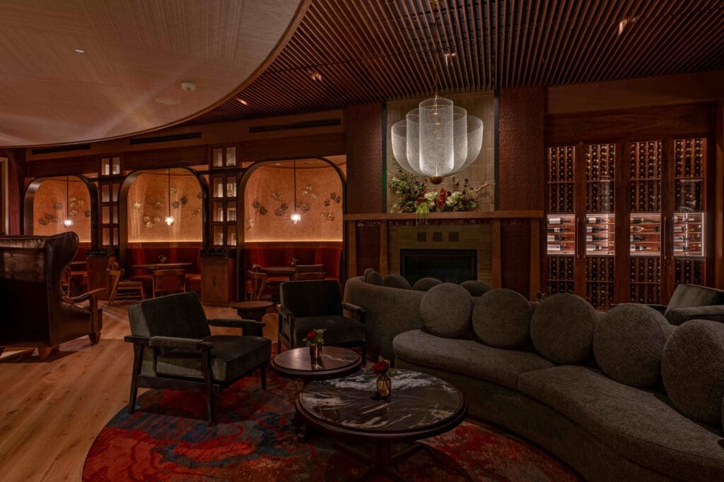 Lounge area inside Napa Rose featuring upholstered sofas, armchairs, fireplace, wine cabinets and soft ambient lighting in a warm-toned interior.