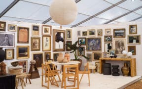 Gallery-style booth at the Marburger Farm Antique Show featuring framed artwork, vintage chairs, sculptural ceramics and wood furniture.