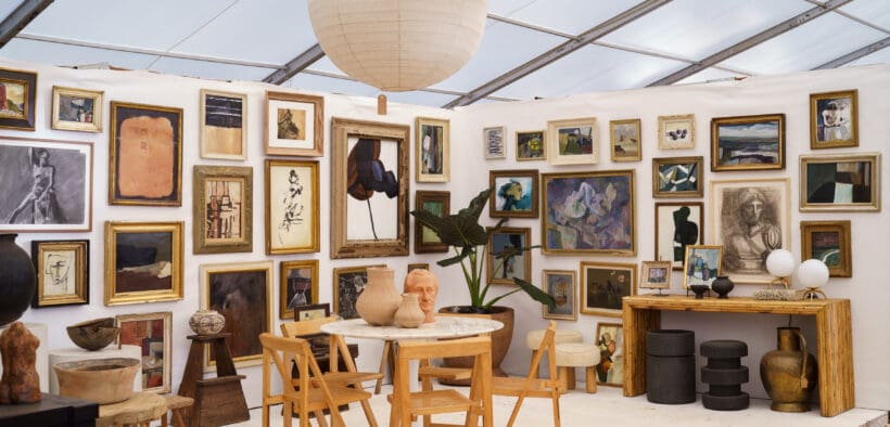 Gallery-style booth at the Marburger Farm Antique Show featuring framed artwork, vintage chairs, sculptural ceramics and wood furniture.