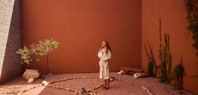 A guest in a robe stands inside a circular stone labyrinth courtyard at Mii amo in Sedona, Arizona, surrounded by terracotta walls, desert landscaping and soft natural light.
