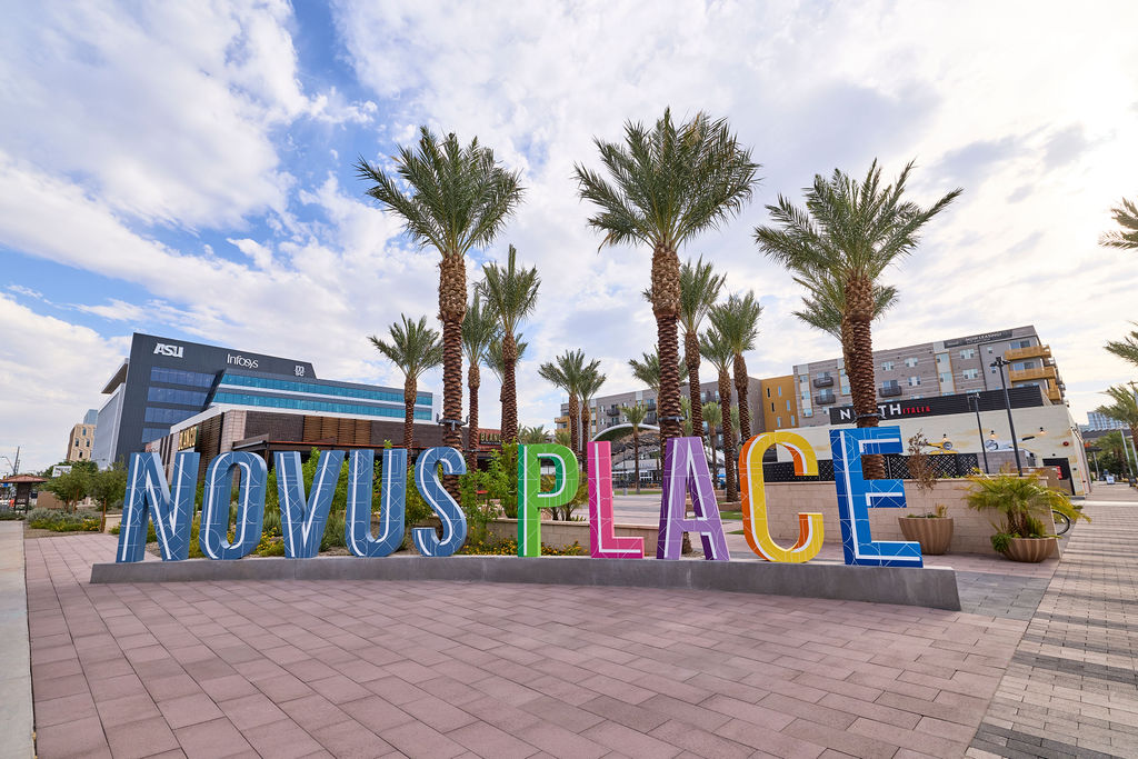 Colorful Novus Place letter sign in a landscaped park area with palm trees and surrounding buildings in Tempe.