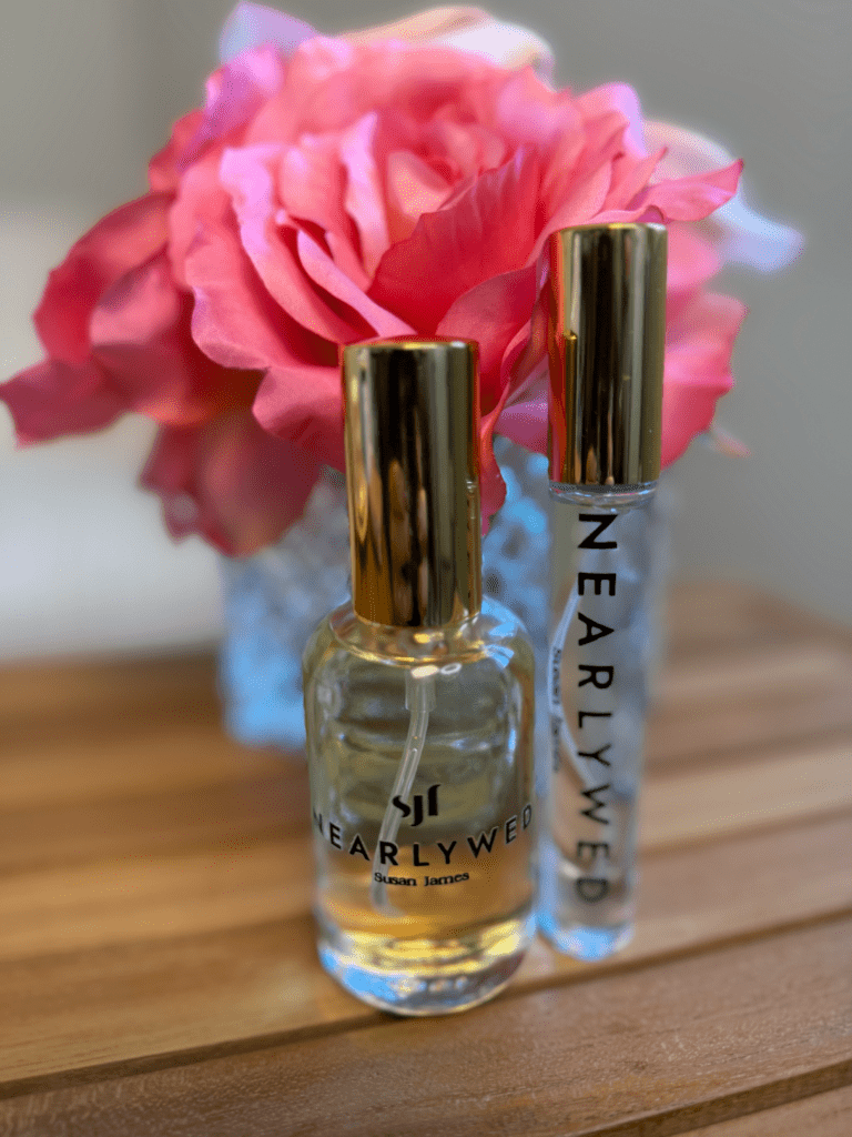Nearlywed perfume by Susan James Fragrances displayed in a glass bottle and travel spray, styled with soft pink florals in the background.