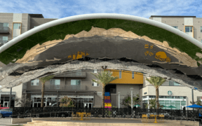 Curved canopy stage at Novus Place in Tempe with green lawn, palm trees and surrounding retail buildings.