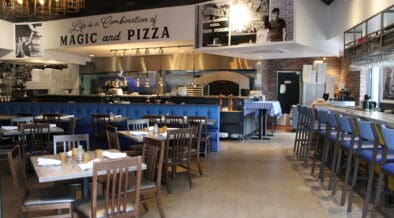 Interior of Patricia’s Pizza in North Scottsdale featuring blue banquettes, wood tables and an open kitchen with a pizza oven.