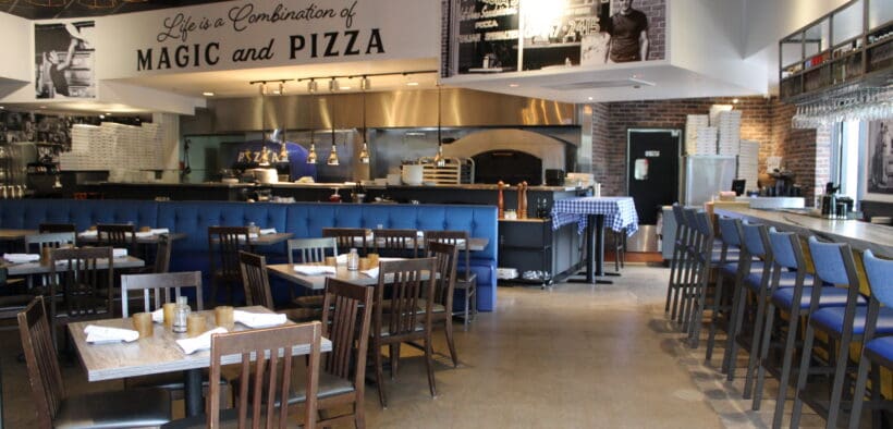 Interior of Patricia’s Pizza in North Scottsdale featuring blue banquettes, wood tables and an open kitchen with a pizza oven.