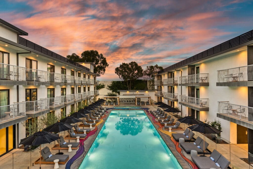Courtyard pool at The Anthem Hotel in Inglewood with lounge chairs, black umbrellas and surrounding guest room balconies at sunset.