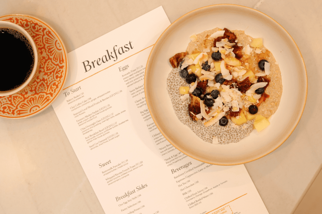 Breakfast bowl topped with fruit, coconut and nuts served beside coffee and a printed menu at Poppy’s in Anaheim.