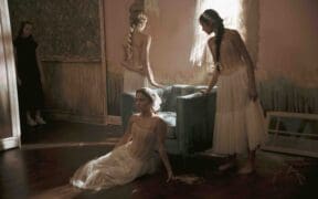 Dancers in soft, neutral costumes pose inside a vintage-style room with textured walls and dramatic lighting in a scene from the Arizona-made cine-dance film Rooms, screening February 24 in Tucson.