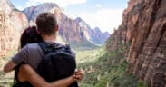 A young couple hugging looking over Zion national park canyon with a cloudy blue sky in the background