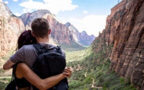 A young couple hugging looking over Zion national park canyon with a cloudy blue sky in the background
