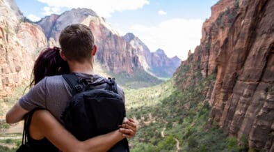 A young couple hugging looking over Zion national park canyon with a cloudy blue sky in the background