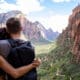A young couple hugging looking over Zion national park canyon with a cloudy blue sky in the background