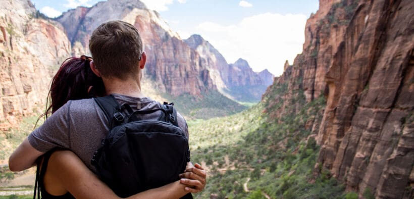 A young couple hugging looking over Zion national park canyon with a cloudy blue sky in the background