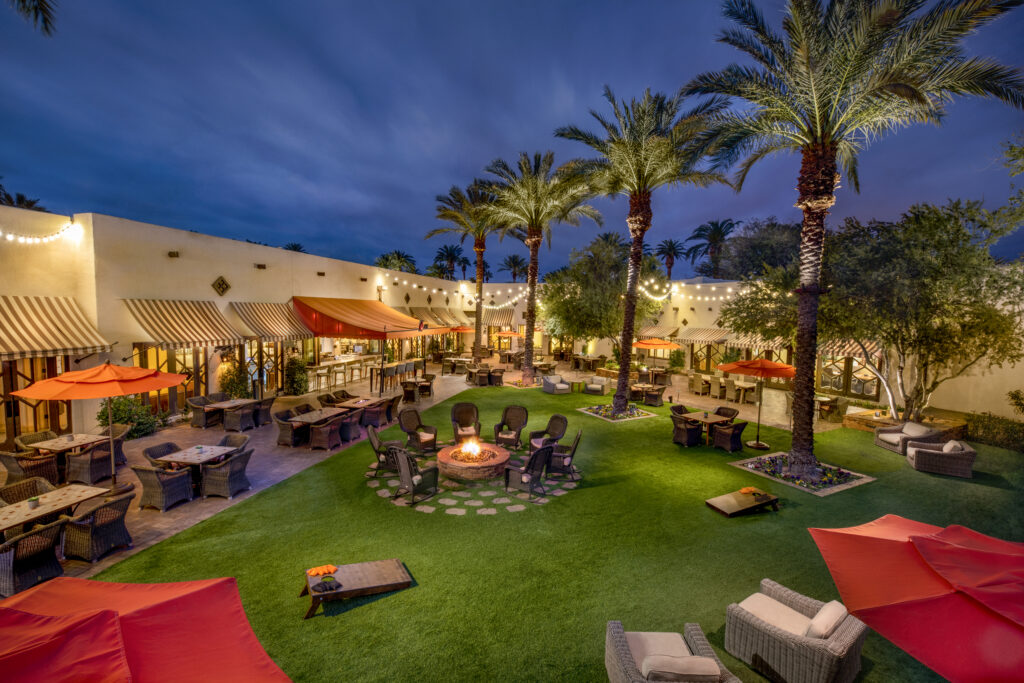 Palm-lined courtyard at The Wigwam illuminated with string lights and fire pits at dusk.
