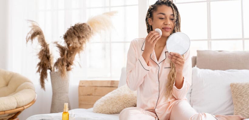 Person enjoying a quiet self-care moment while applying skincare in a softly lit bedroom, reflecting indulgent Valentine’s Day rituals.