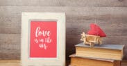 Framed artwork reading “love is in the air” displayed on a wooden surface beside stacked books and a small red heart decoration, representing sentimental Valentine’s Day gifts.