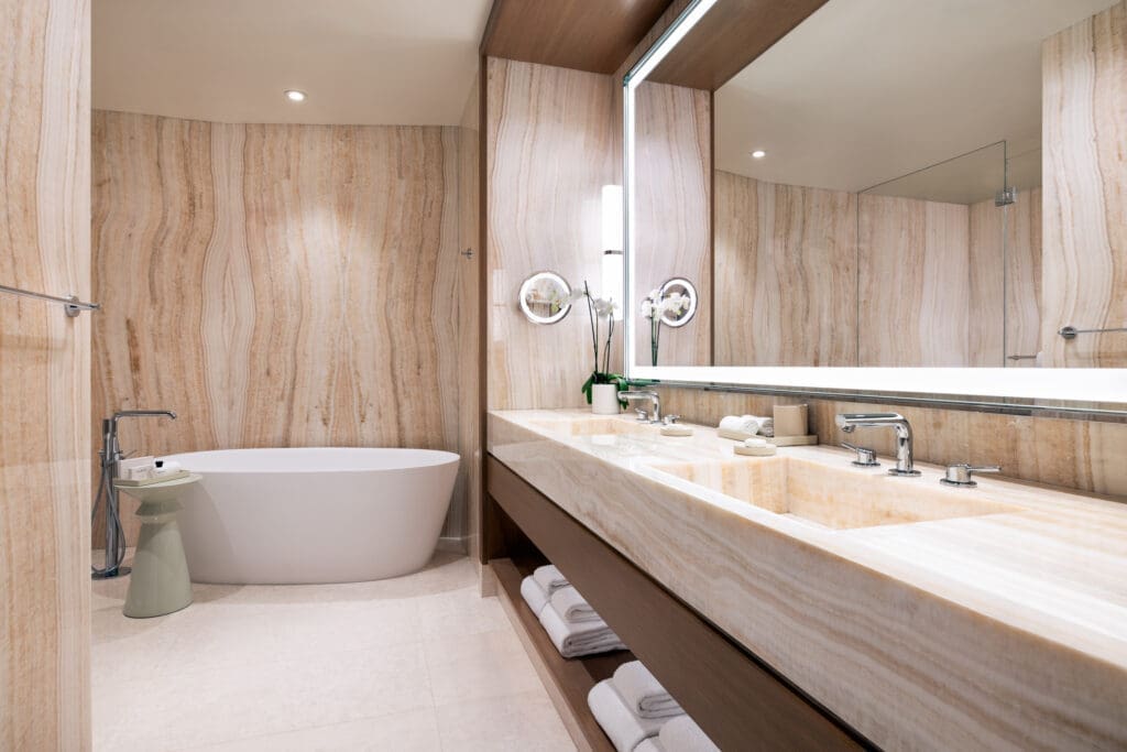 Luxury Patio Suite bathroom at Green Valley Ranch with freestanding soaking tub, marble vanity and large illuminated mirror.