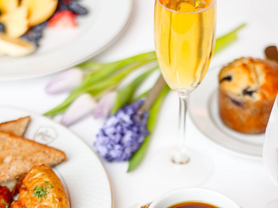 Elegant brunch setting with champagne, pastries, potatoes and toast and fresh flowers on a white table.