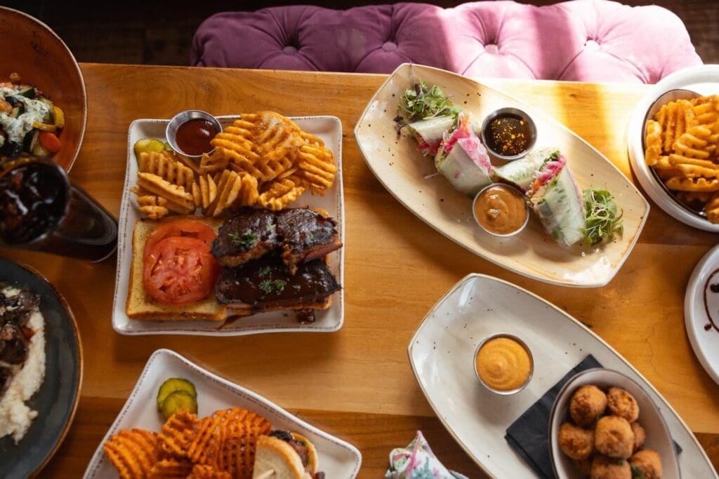 Overhead view of a restaurant table with burgers, waffle fries, spring rolls, dipping sauces and multiple shared plates during Easter brunch at Bird & Jim. 