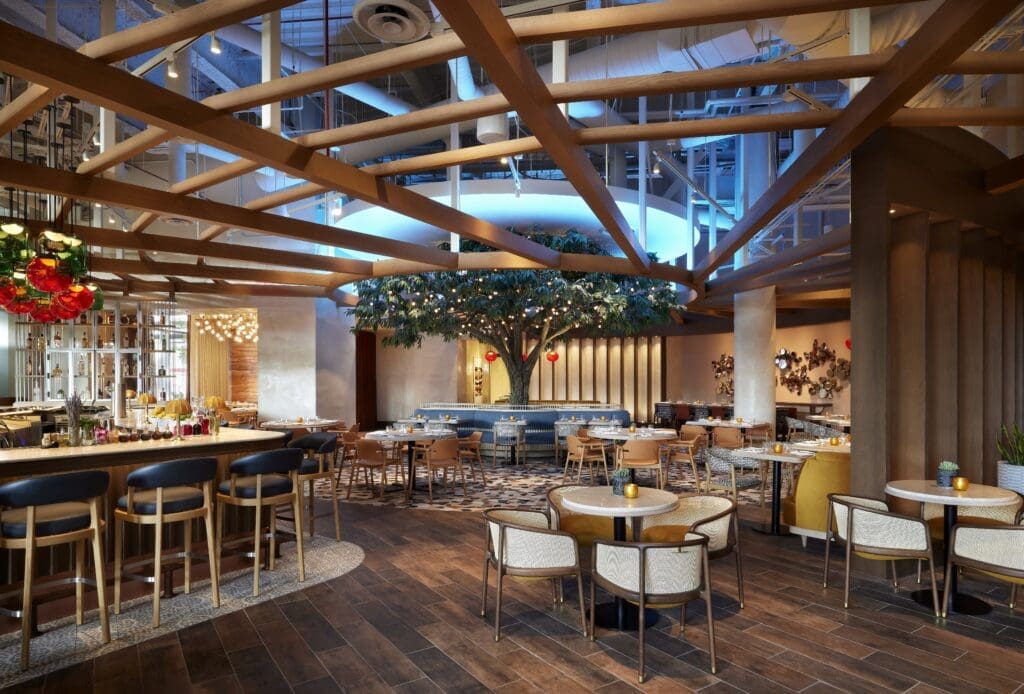 Sheraton Denver Downtown Carcara restaurant interior featuring wood beams, a central tree installation and warm ambient lighting.