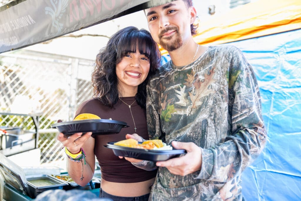 Two festival guests smile while holding plates of food at a vendor booth during the Spirits of Mexico Festival in Downtown Phoenix.