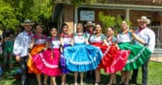 A group of folklórico dancers wearing brightly colored dresses and traditional attire pose together in front of a historic building at Heritage Square in Phoenix.