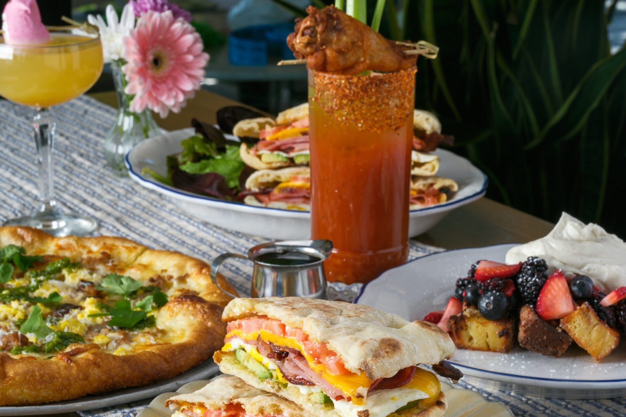 Brunch table with breakfast sandwich, pizza, cocktails and fresh fruit arranged on a patio setting at Doughbird.
