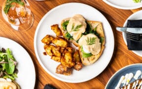 Overhead view of eggs benedict with hollandaise sauce, roasted potatoes and greens on a white plate at Apple Blossom's Easter brunch.