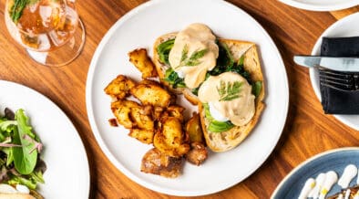 Overhead view of eggs benedict with hollandaise sauce, roasted potatoes and greens on a white plate at Apple Blossom's Easter brunch.