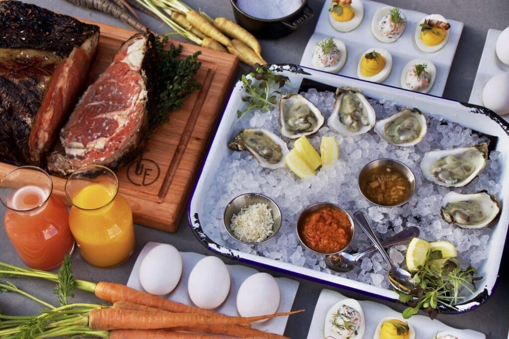 Raw oysters on ice with sauces and lemon alongside deviled eggs, carrots, juices and a large cut of beef on a buffet spread at the Urban Farmer at The Oxford Hotel.