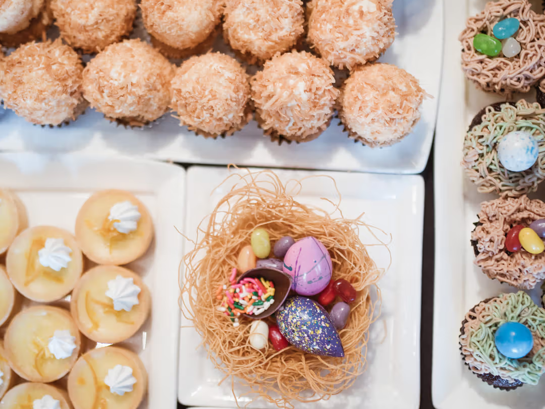 Assorted Easter desserts including cupcakes decorated like nests, coconut macaroons, mini tarts and chocolate treats arranged on white platters with colorful candy eggs at Element 47 at The Little Nell.