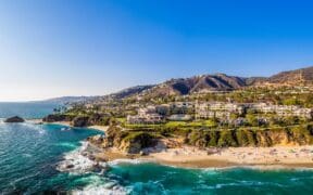 Aerial view of Laguna Beach coastline with turquoise water, sandy beach and hillside homes.