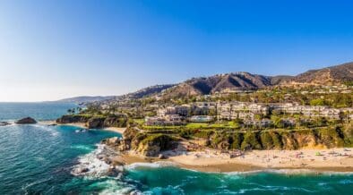 Aerial view of Laguna Beach coastline with turquoise water, sandy beach and hillside homes.