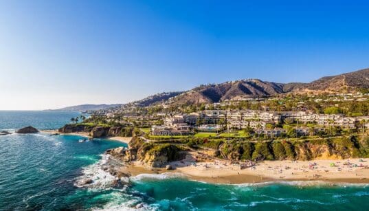 Aerial view of Laguna Beach coastline with turquoise water, sandy beach and hillside homes.