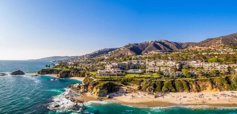 Aerial view of Laguna Beach coastline with turquoise water, sandy beach and hillside homes.