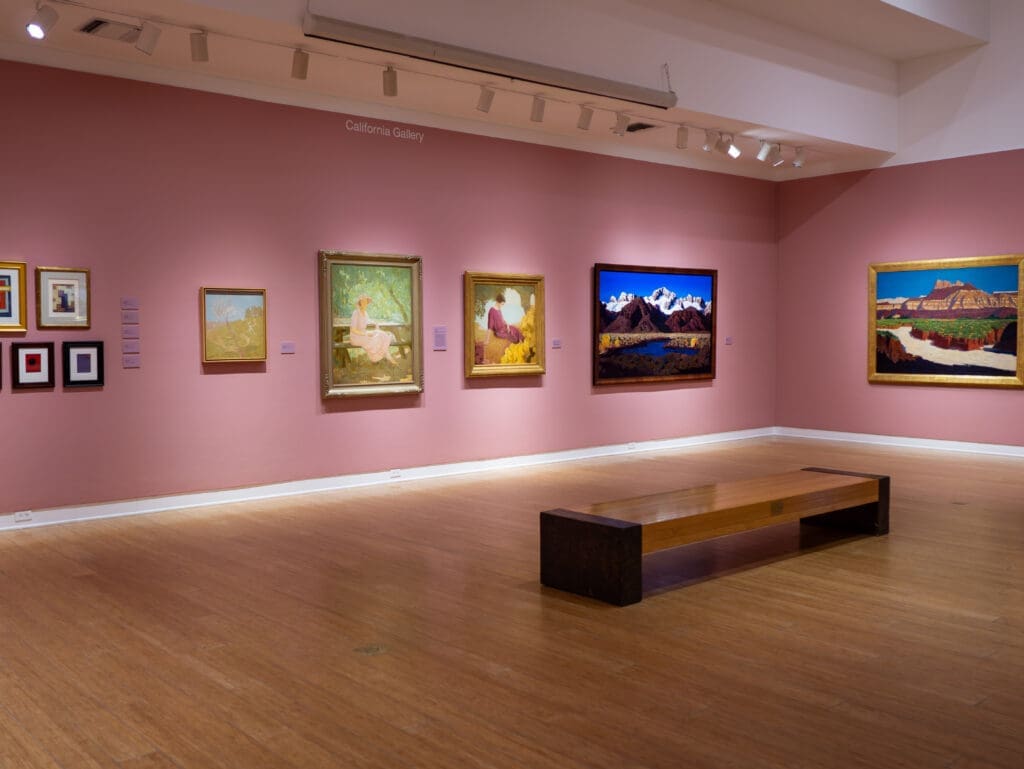 Interior of an art gallery with paintings displayed on pink walls in Laguna Beach.