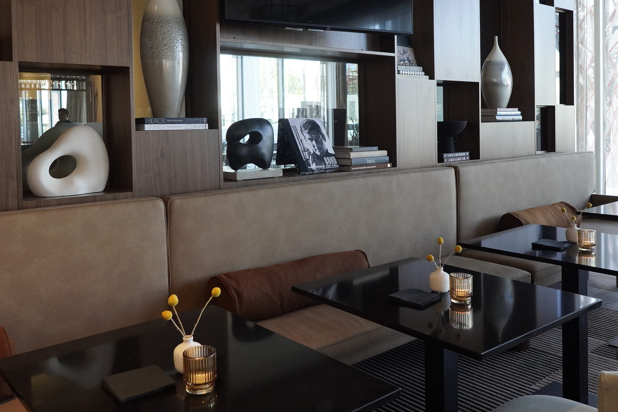 AC Lounge seating area with built-in wood shelving, decorative vases and intimate table settings.