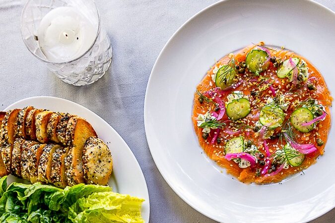 Overhead view of brunch dishes including roasted potatoes, salad, sliced bread and glazed meat plates on a white tablecloth.