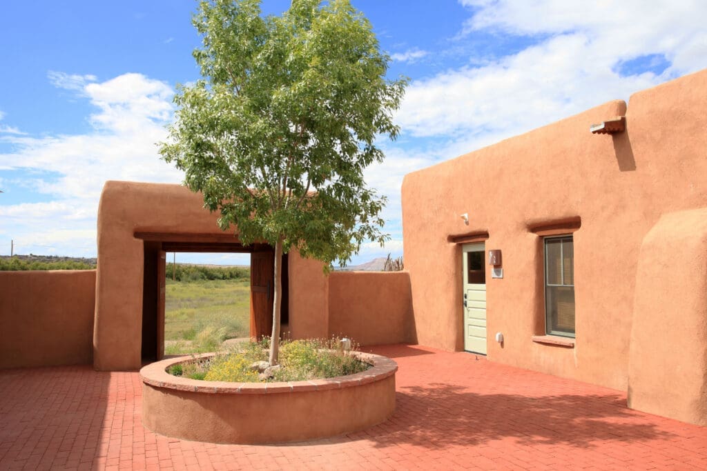 Adobe-style building with courtyard and tree in a peaceful New Mexico landscape.