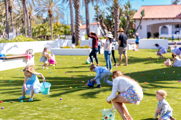 Children and families participating in an outdoor Easter egg hunt on a grassy lawn, collecting colorful eggs in baskets at Omni La Costa Resort & Spa.