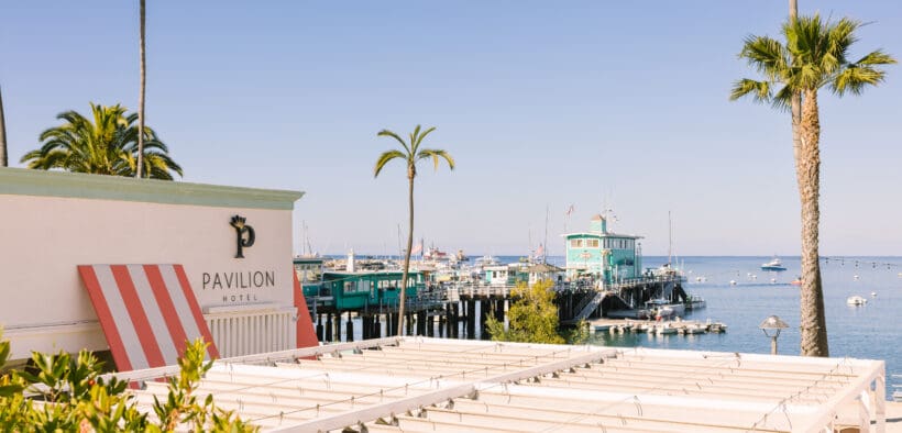 Pavilion Hotel exterior in Avalon with ocean view, palm trees and Catalina Island harbor showcasing waterfront hotel location Southern California.