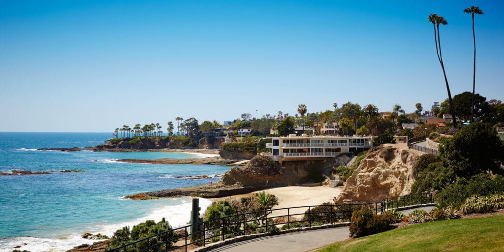 Coastal view of Laguna Beach cliffs with oceanfront homes and sandy cove below.